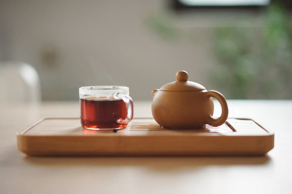 tea pot and glass tea cup on wooden tray